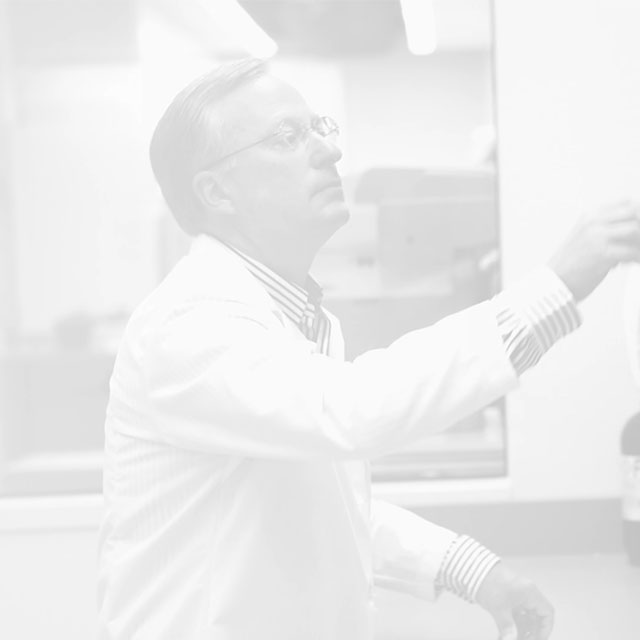 Faded black and white photo of Dr. Samuel Lynch reaching for an item in a lab.