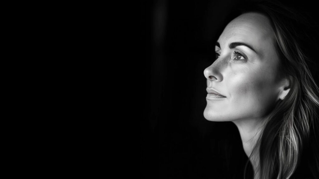 A black and white portrait of a woman's face in profile on a black background